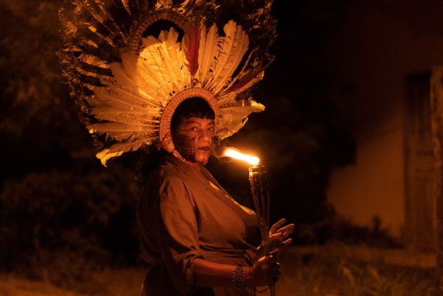 Eine indigene Person mit Kopfschmuck hält eine Flamme
