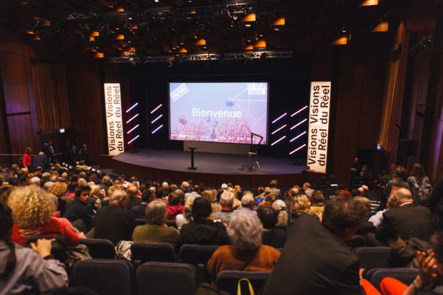 Ein Kinosaal mit viel Publikum von hinten, Bildschirm zeigt Bienvenue 2022